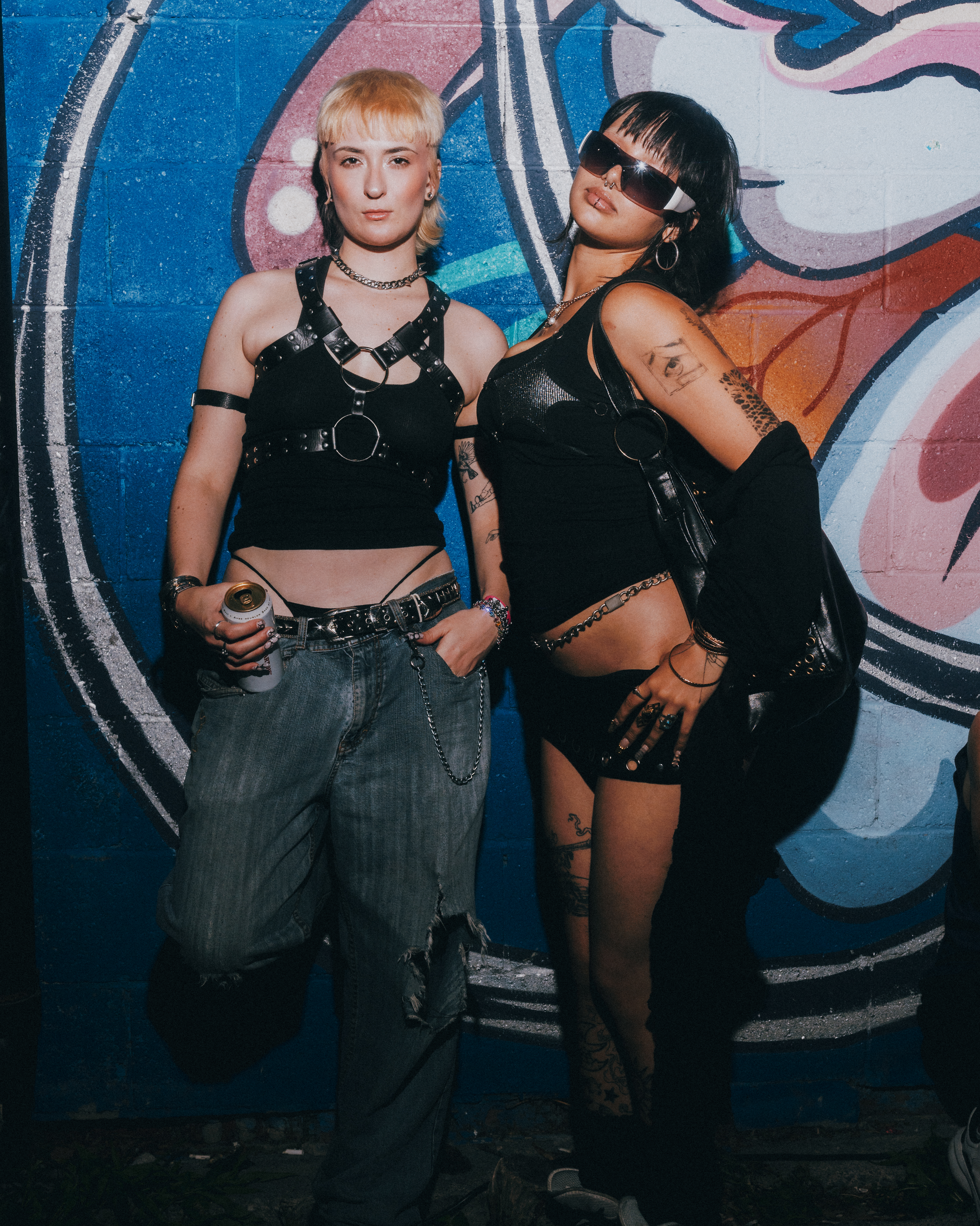 Two Pep Rally guests posing together in black outfits against a colourful mural