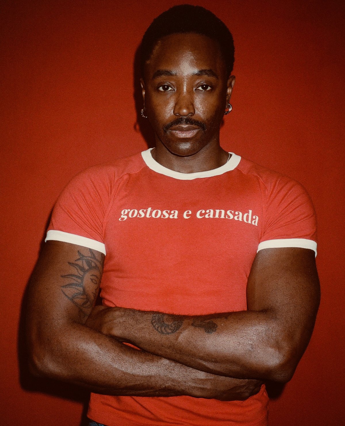 Portrait of Karim Olen Ash with arms crossed against a red backdrop