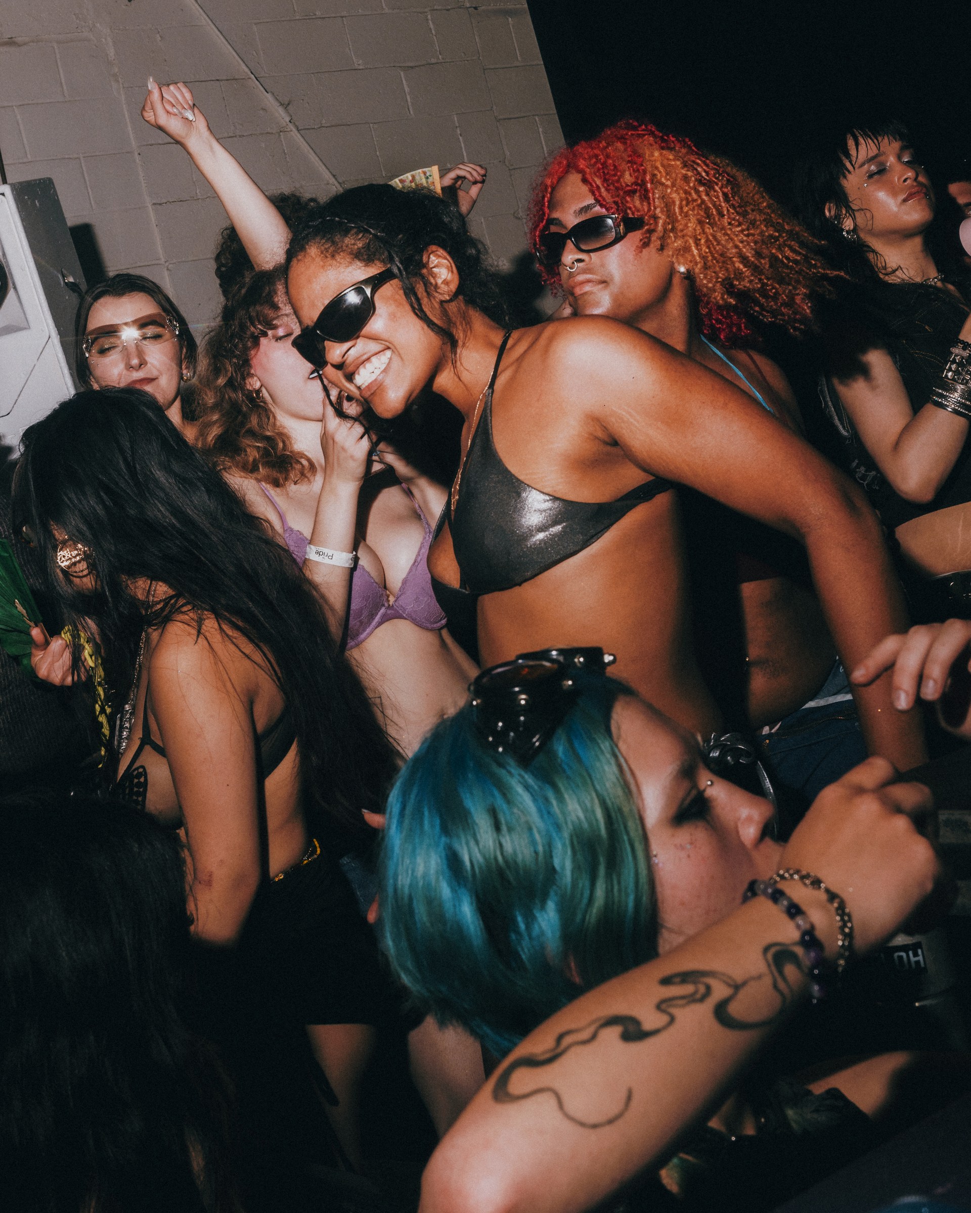 Close-up of a dancing Pep Rally crowd, with a smiling person in sunglasses and a black top and a blue-haired attendee in the foreground